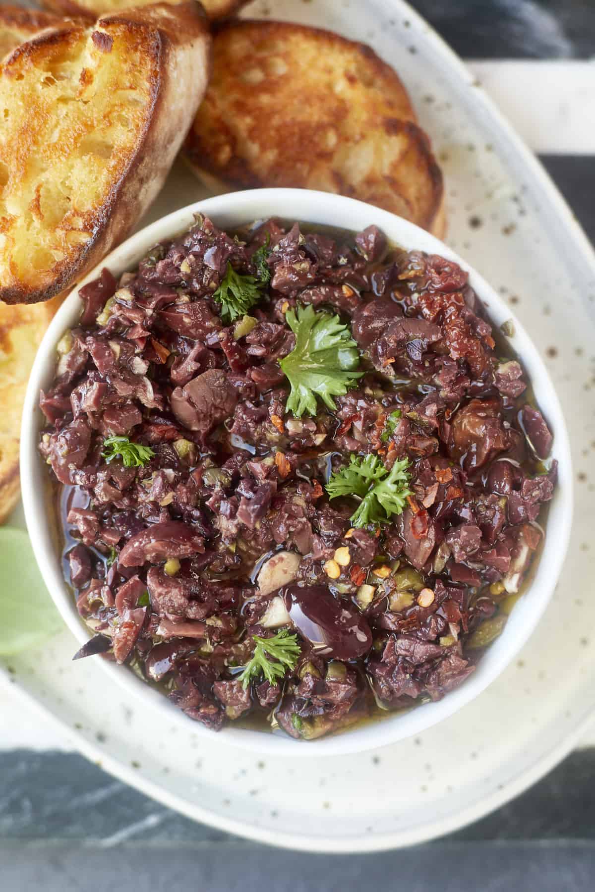 olive tapenade in a bowl with toasted bread in the background