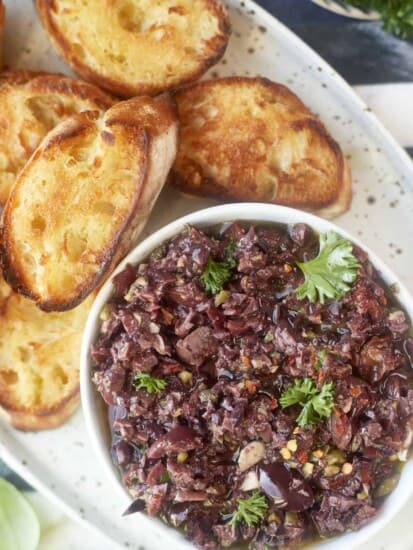 overhead image of a platter with a bowl of easy olive tapenade and toasted crostini