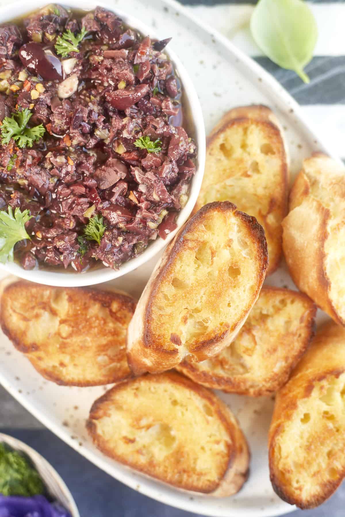 a platter with a bowl of easy olive tapenade and toasted crostini