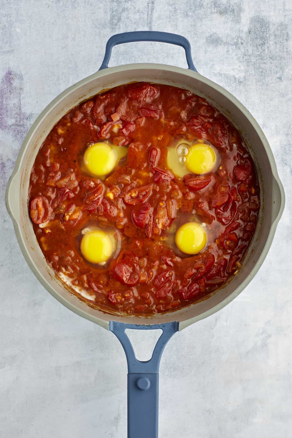 four eggs cracked into shakshuka sauce in a large pot