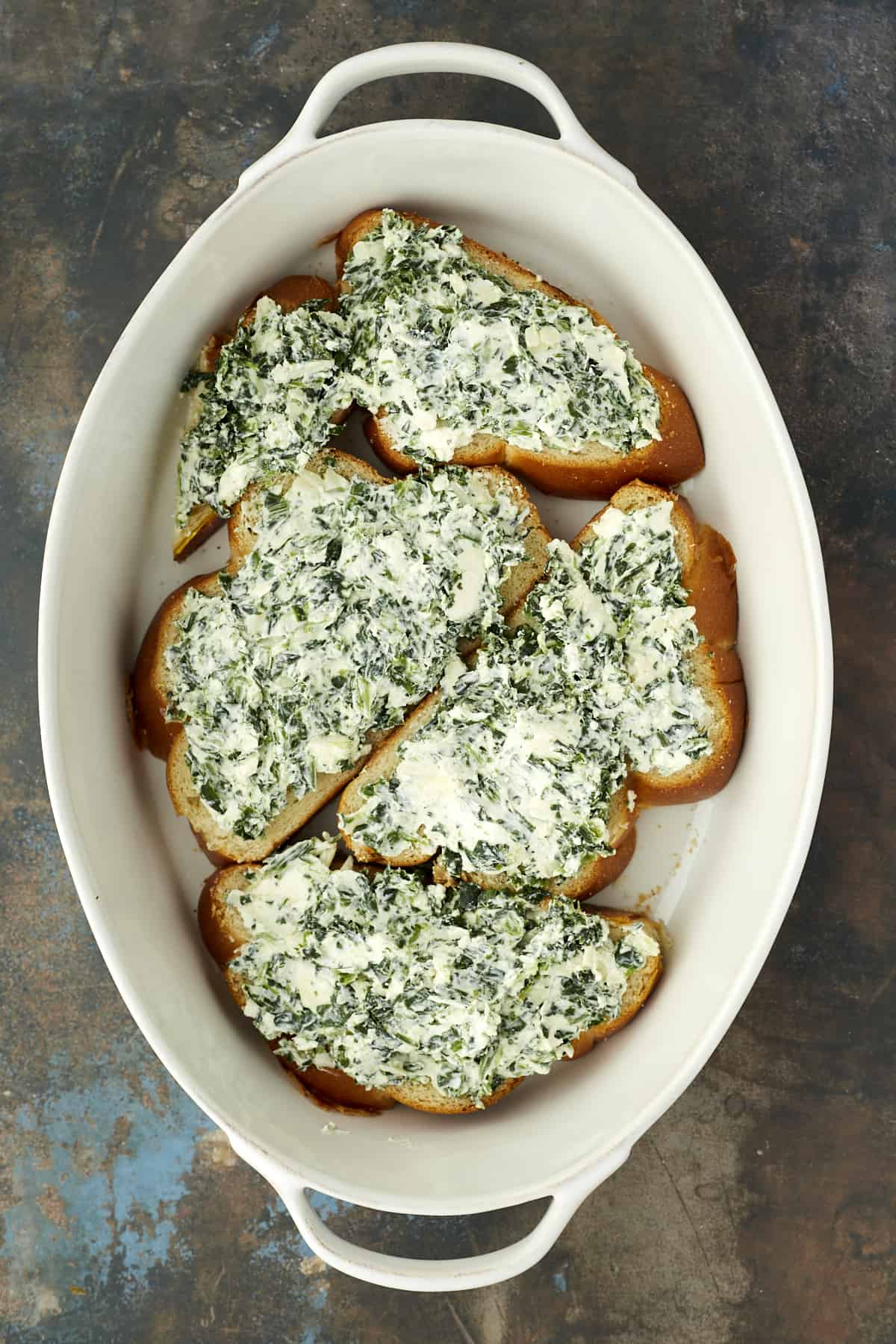overhead image of 4 slices of bread in the bottom of a baking dish topped with a spanakopita spinach filling