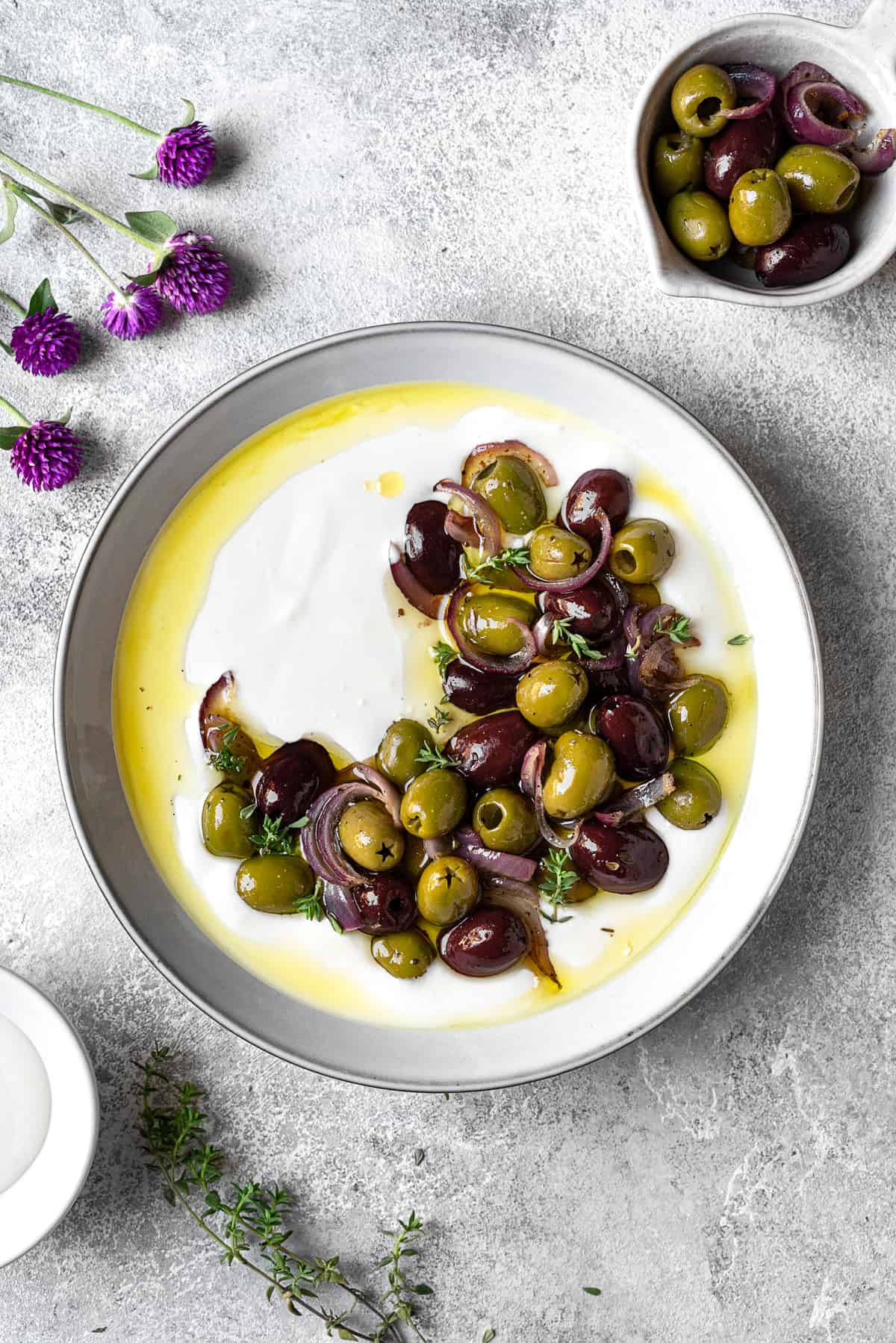 gray plate with whipped feta topped with roasted olives and garnished with fresh parsley and olive oil