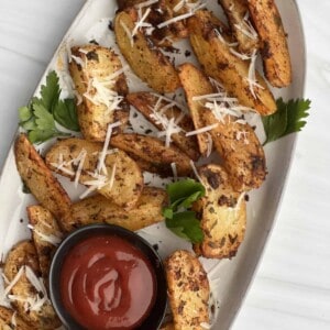 a platter of air fryer garlic parmesan potato wedges with a small container of ketchup in the middle