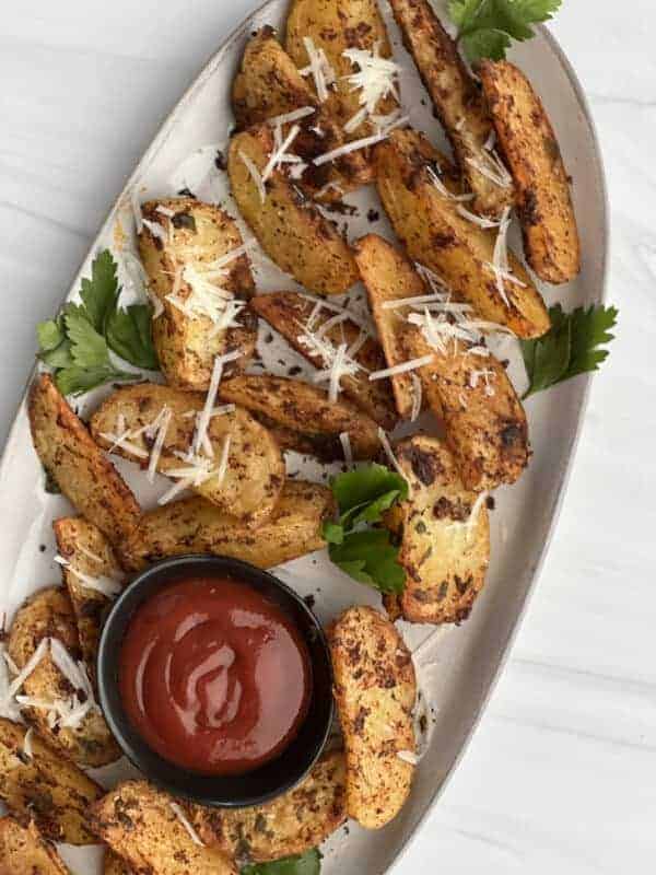 a platter of air fryer garlic parmesan potato wedges with a small container of ketchup in the middle.