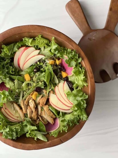 overhead image of a wooden bowl full of Fall Harvest Salad with Honey Balsamic Vinaigrette with two serving spoons on the side