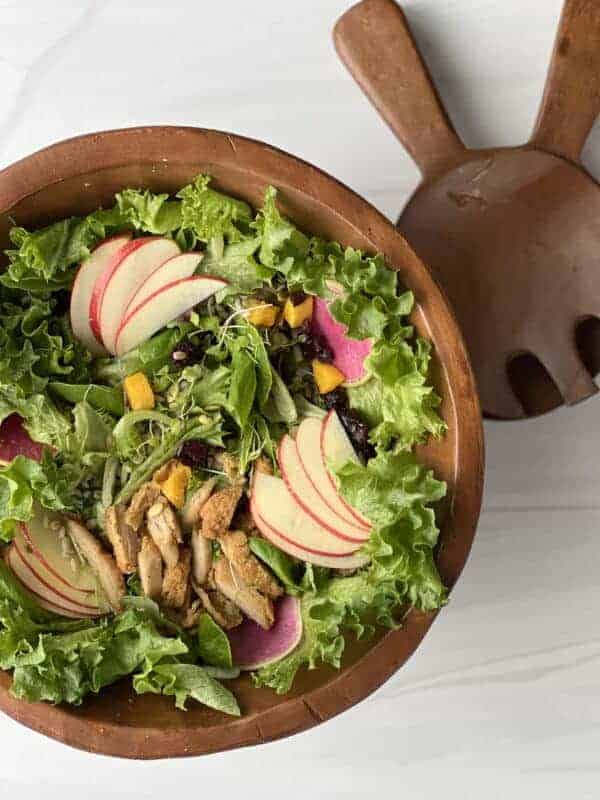 Fall harvest salad with apples, butternut squash, and dried cranberries in a wooden bowl with serving spoons on the side