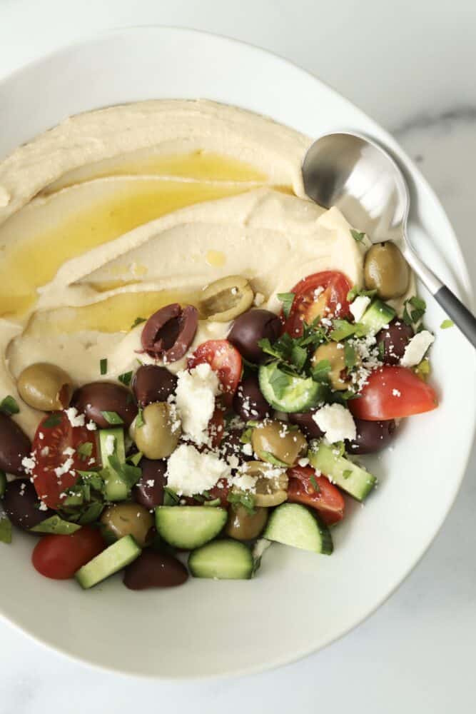 a bowl of hummus topped with olive oil roasted tomatoes and olives and feta