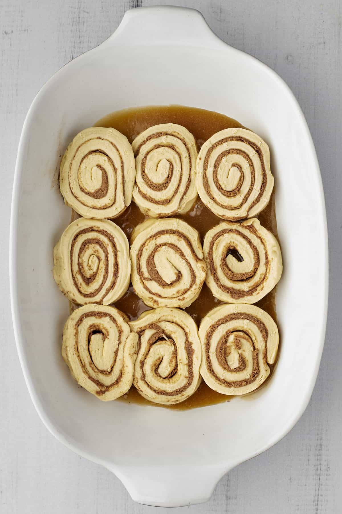 unbaked cinnamon rolls on top of caramel sauce in a white baking dish