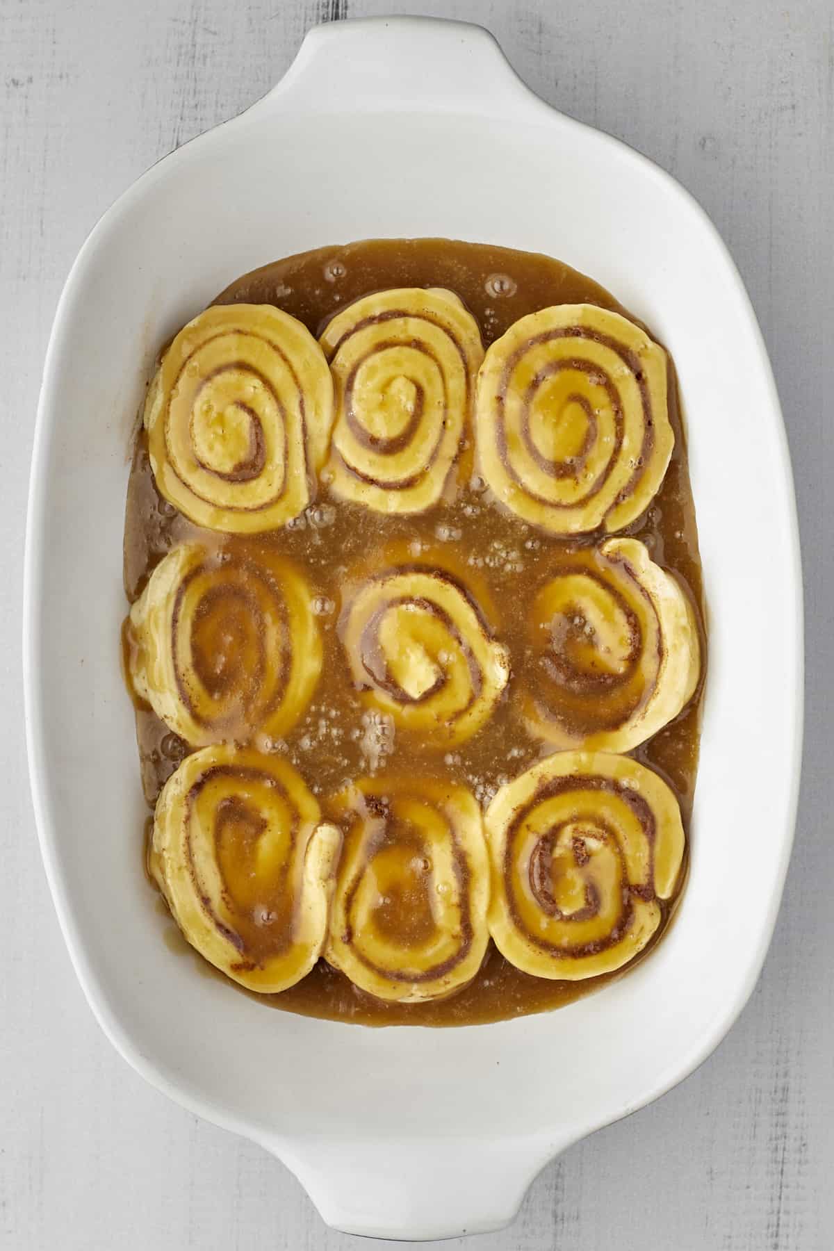 unbaked cinnamon rolls in between layers of homemade caramel sauce