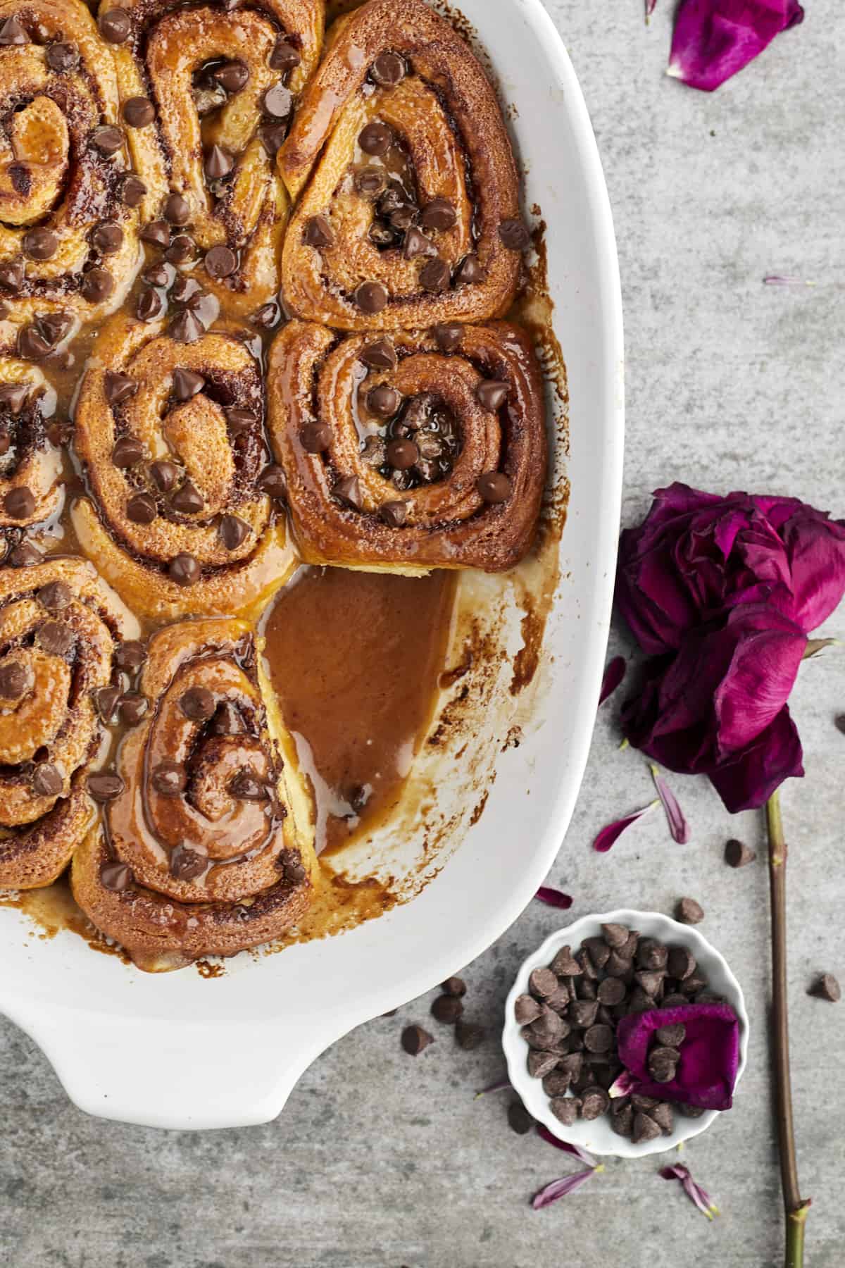 baked easy cinnamon rolls topped with caramel and chocolate chips in a white baking dish with one cinnamon roll missing