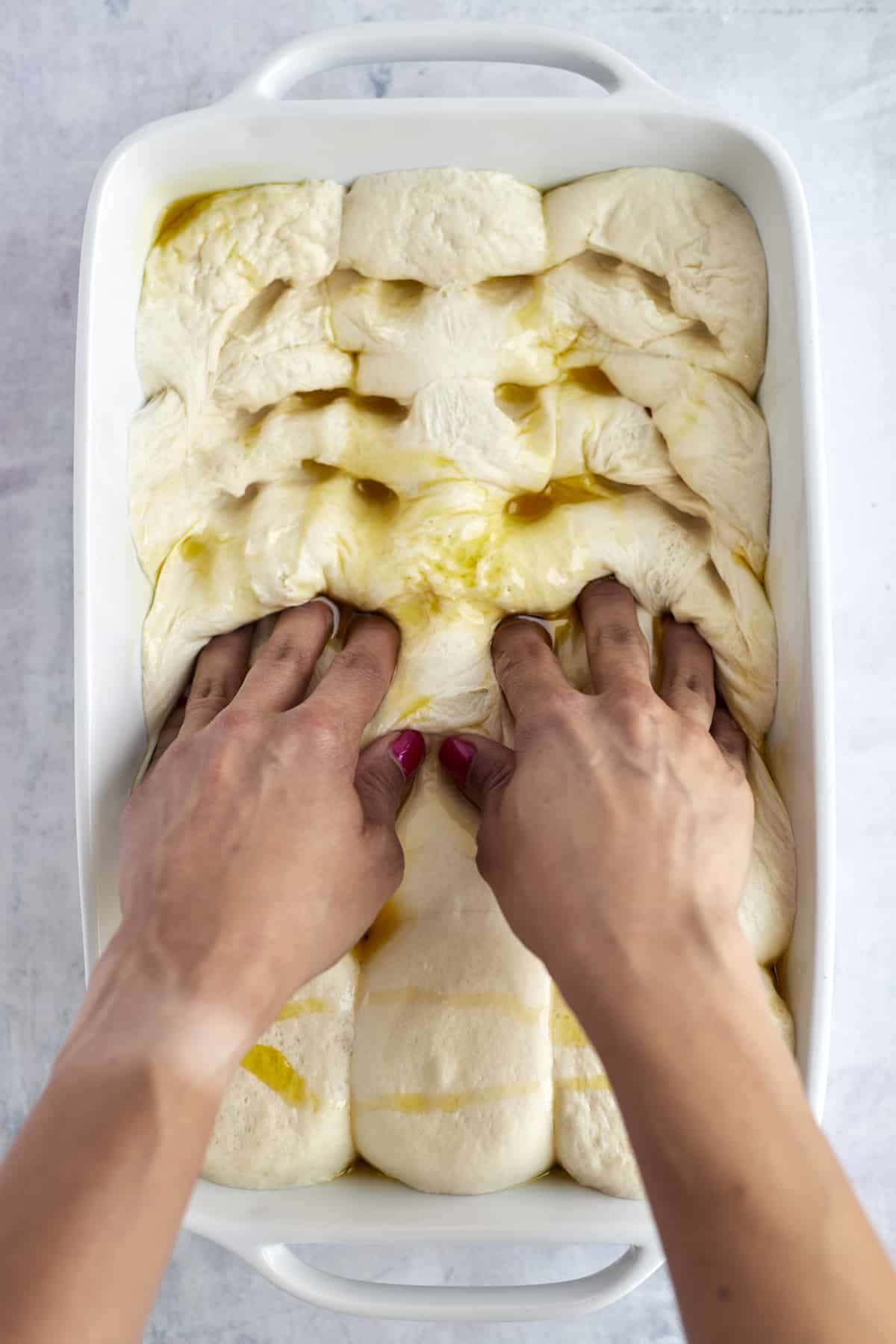 fingers pressing indents into raw dough topped with olive oil