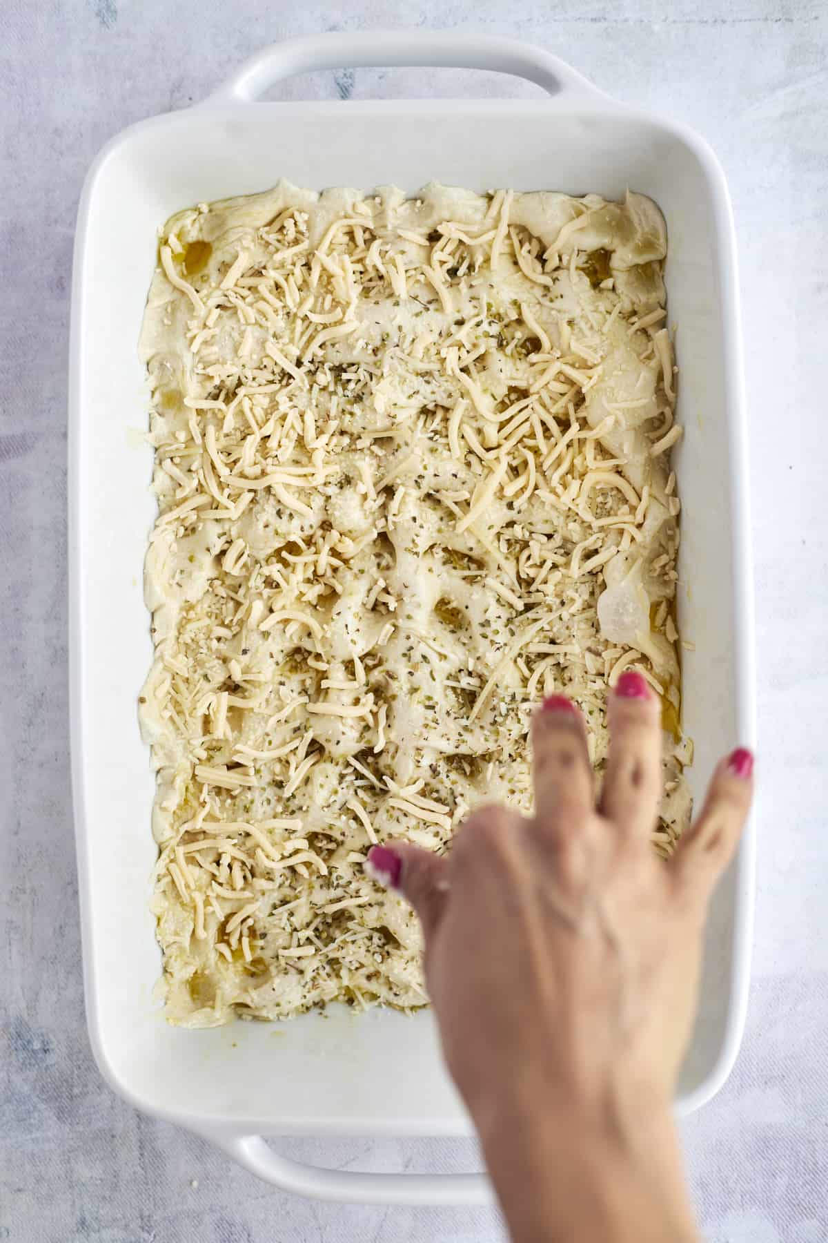 cheese being sprinkled over unbaked focaccia bread rolls