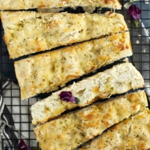 pieces of no knead cheesy focaccia bread on a cutting board with fresh basil.