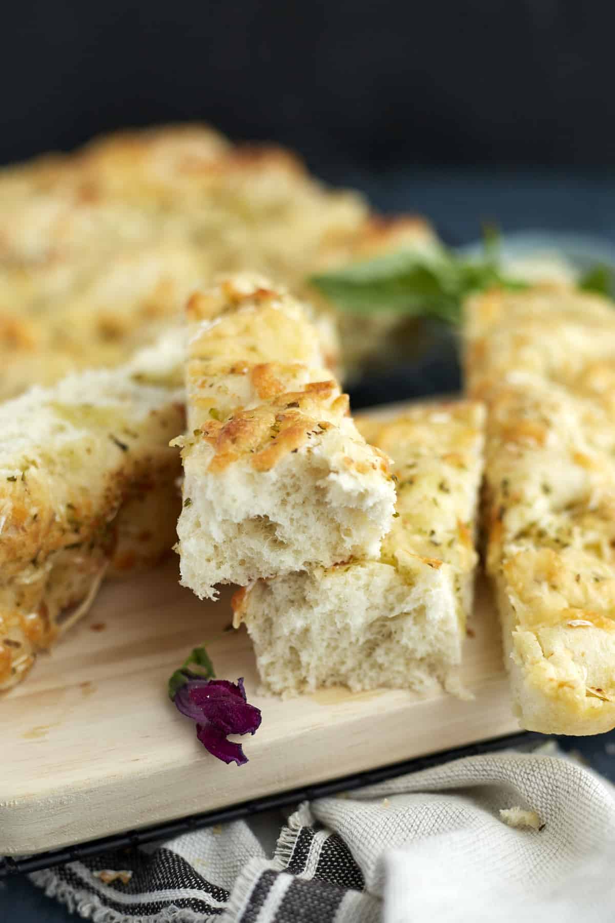 pieces of no knead cheesy focaccia bread on a cutting board with fresh basil.