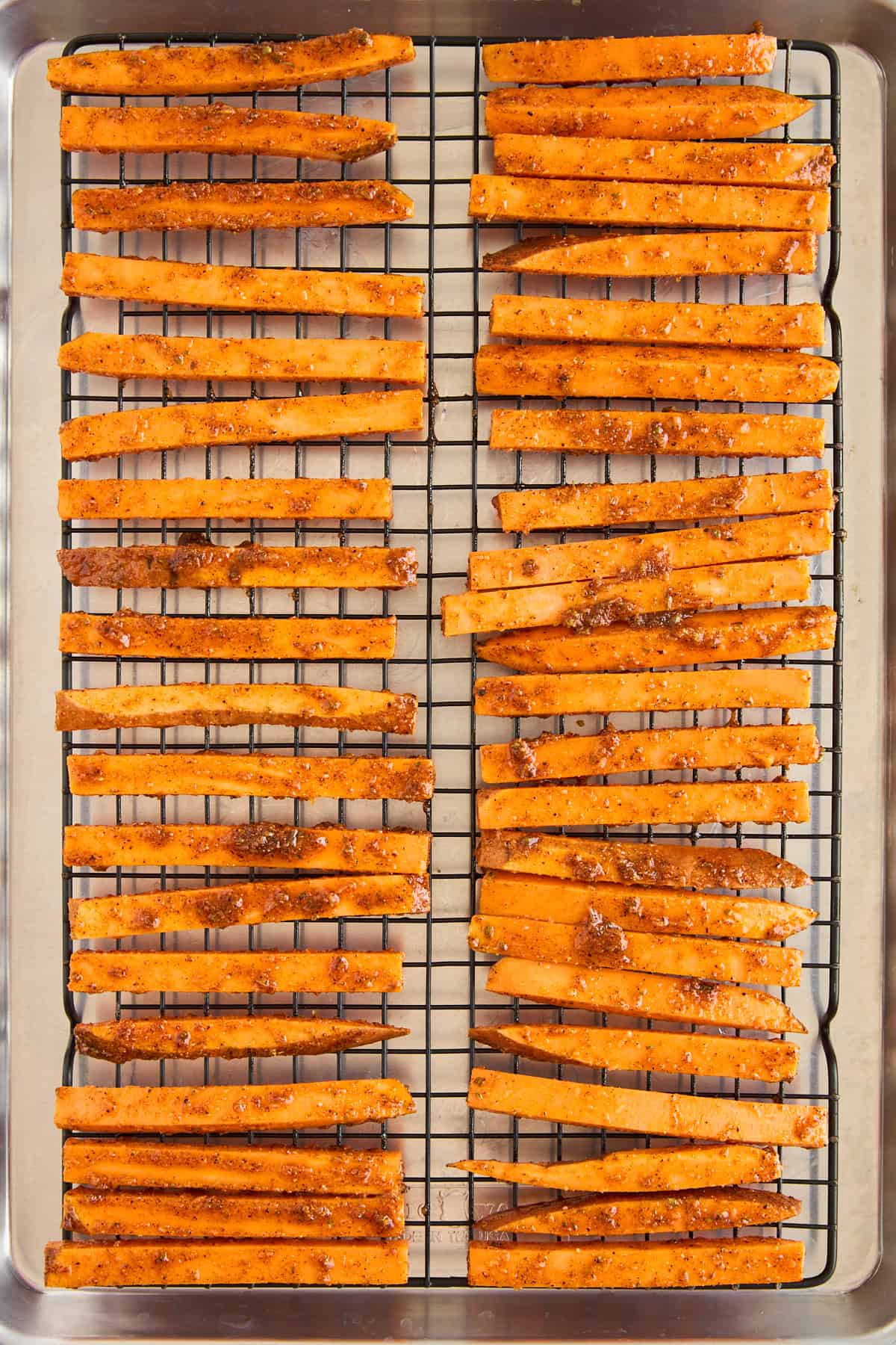 Raw seasoned sweet potato fries on a wire rack on a baking sheet.