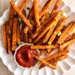 A plate of oven baked sweet potato fries with a cup of ketchup.