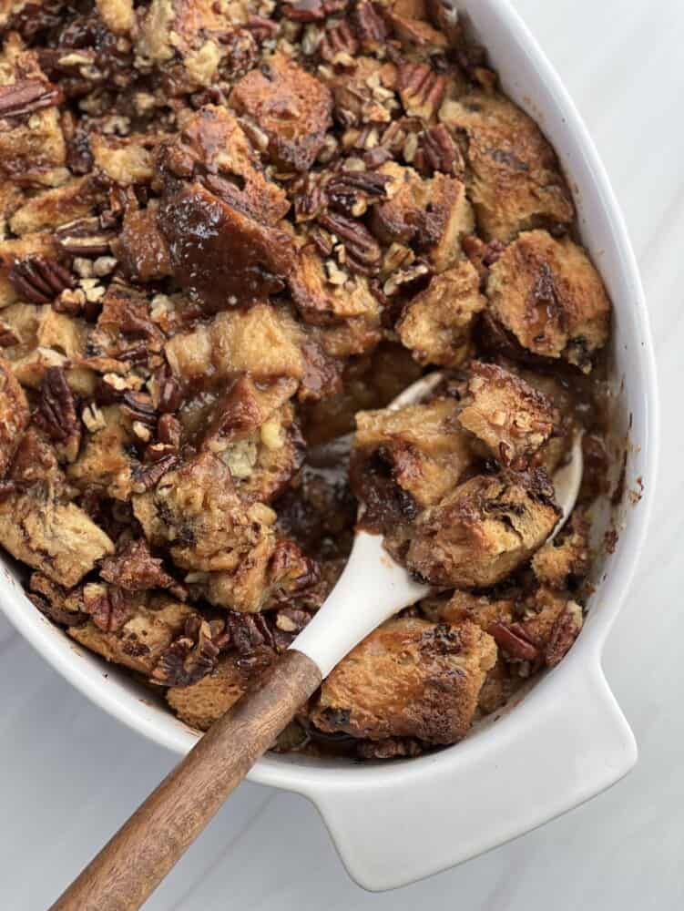 a baking dish of panettone bread pudding with pecan pie filling with a spoon lifting a serving.