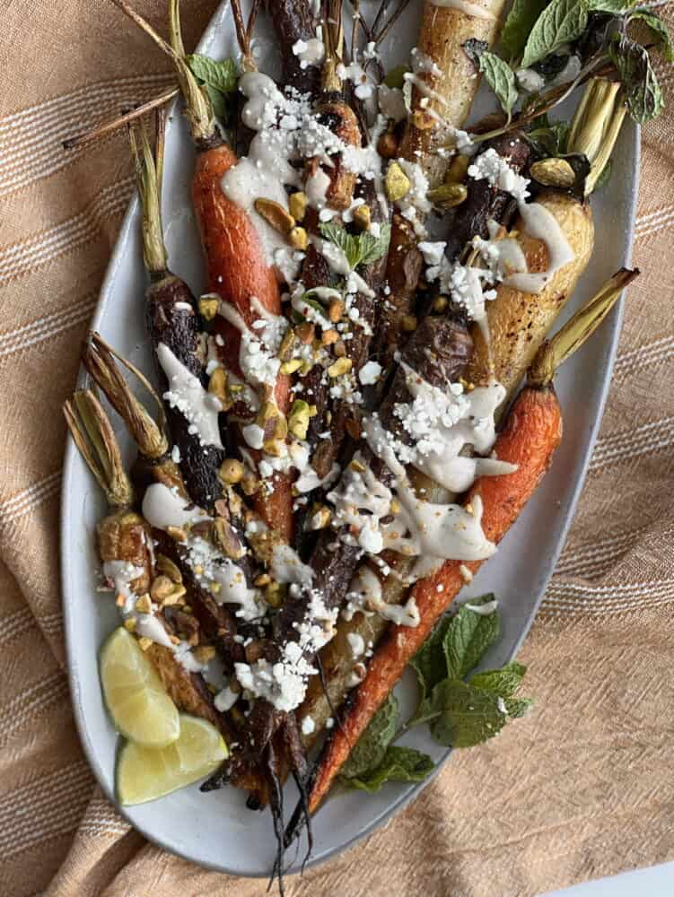 a platter of oven roasted whole carrots topped with tahini dressing