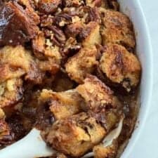 close up image of a spoon scooping a serving of panettone bread pudding from a baking dish.