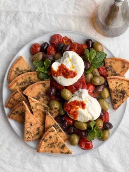 close up burrata with roasted tomatoes, olives and zaatar pita