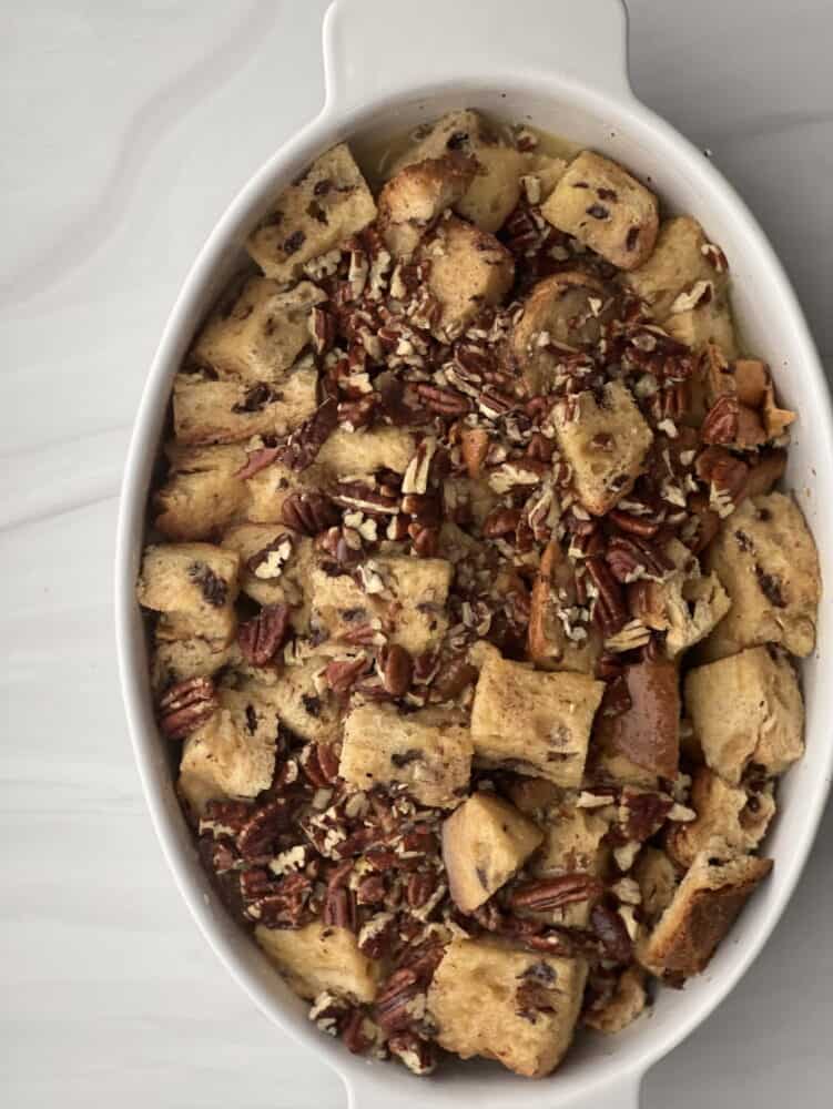 overhead image of unbaked panettone bread pudding with pecan pie filling in an oval baking dish 
