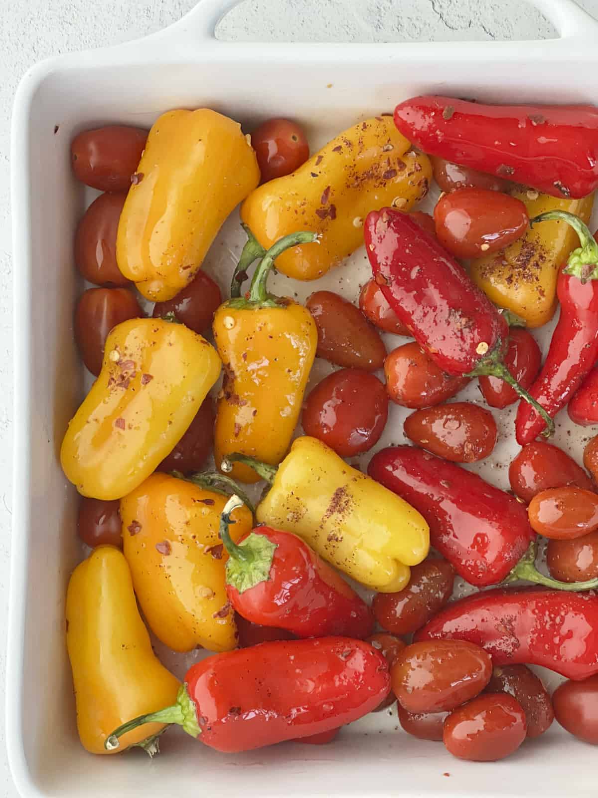 peppers and tomatoes in a baking dish coated with oil and seasonings