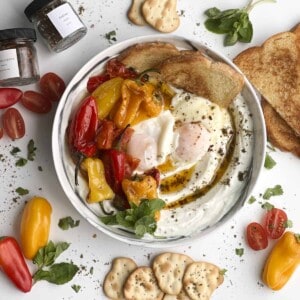 a bowl of turkish eggs with yogurt, toast, and roasted peppers and tomatoes