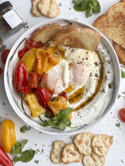 a bowl of turkish eggs with yogurt, toast, and roasted tomatoes and peppers