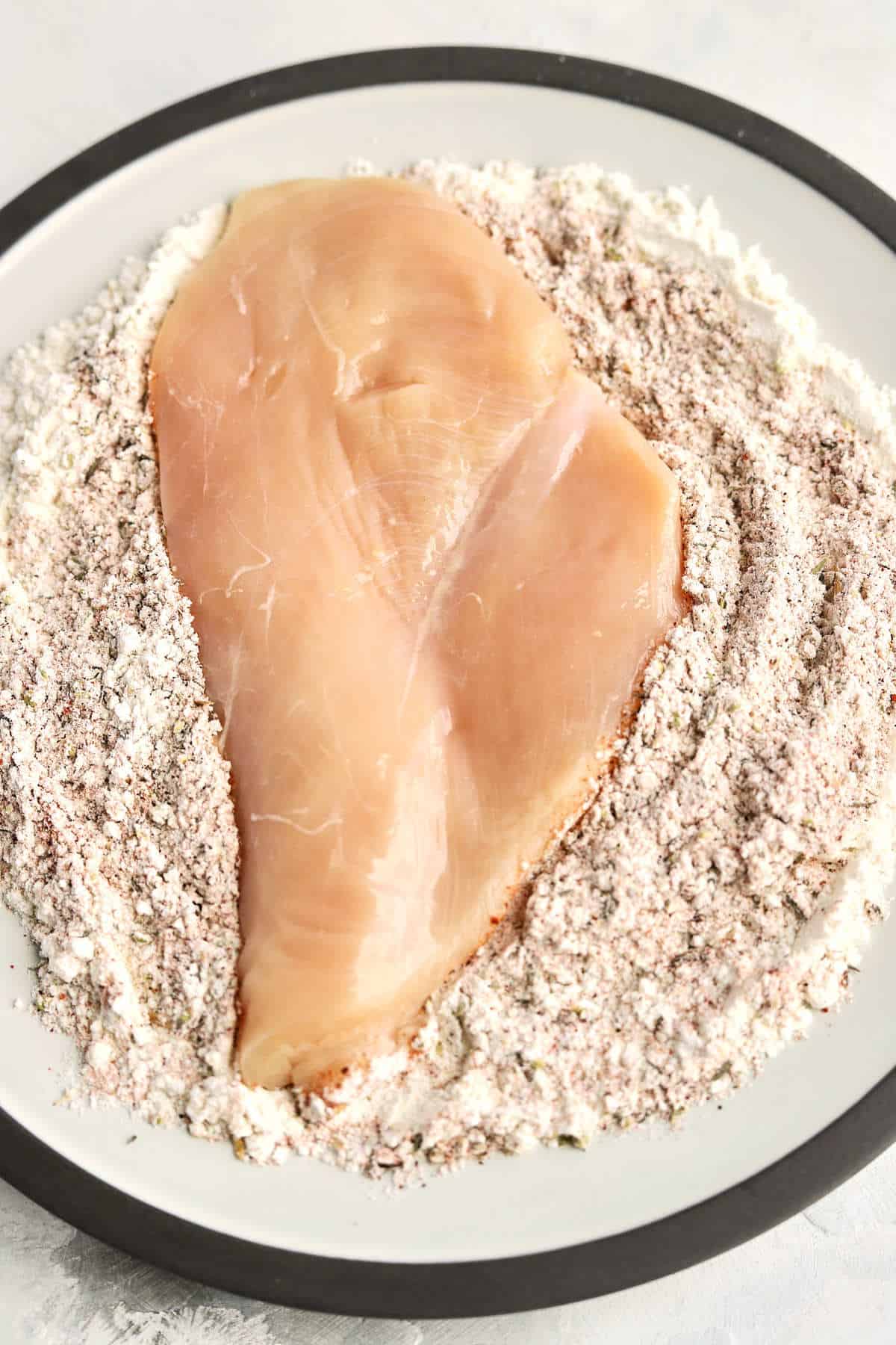 Raw chicken in a bowl on top of spiced flour. 