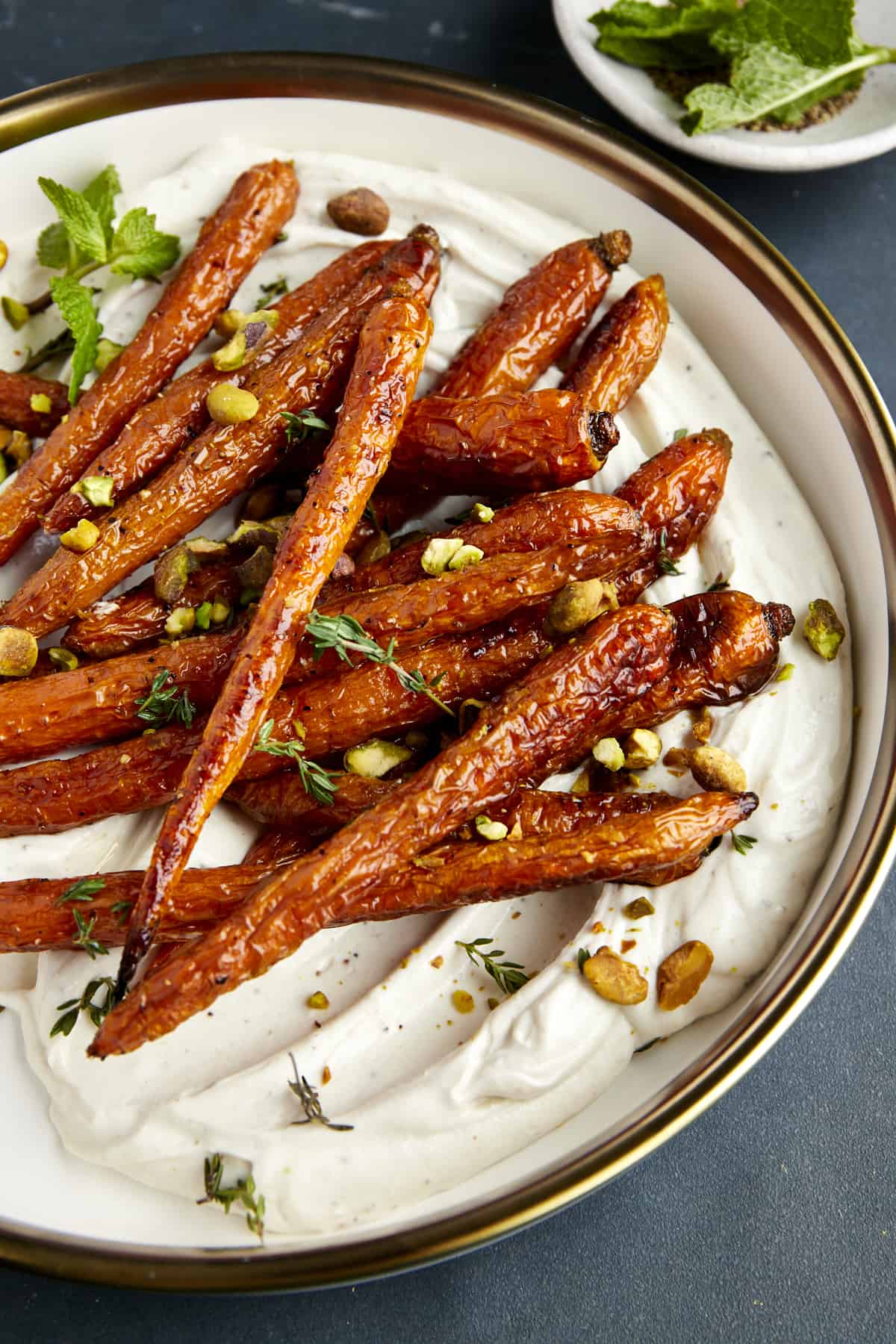 A bowl of roasted carrots with tahini dressing topped with pistachios and mint. 