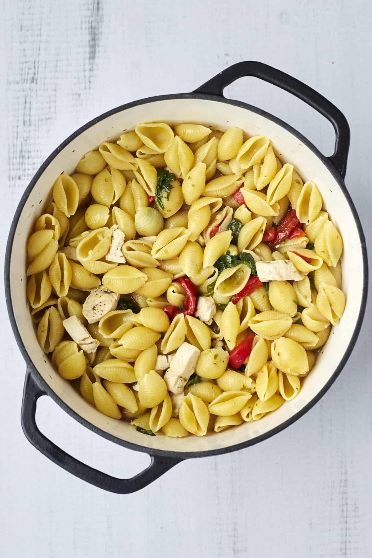 Cooked pasta shells, spinach, red bell peppers, roasted peppers, and chicken in a pot.