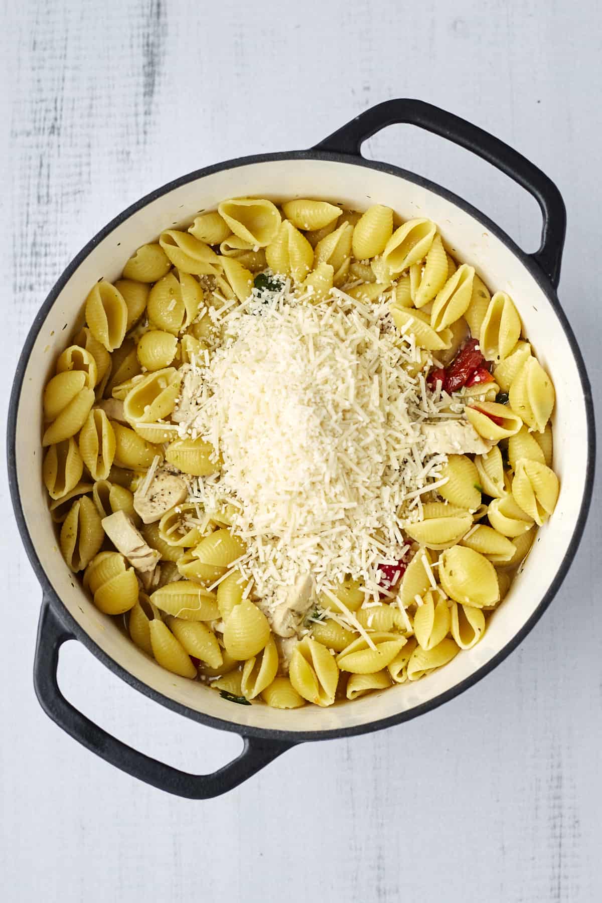 Freshly grated Parmesan on top of creamy tuscan chicken pasta in a large pot.