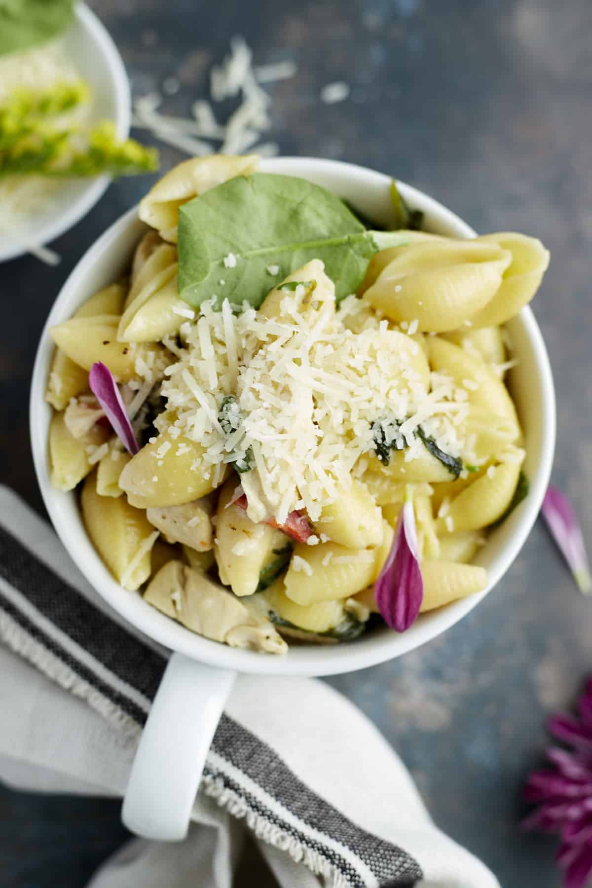 A mug full of creamy tuscan chicken pasta topped with grated Parmesan.