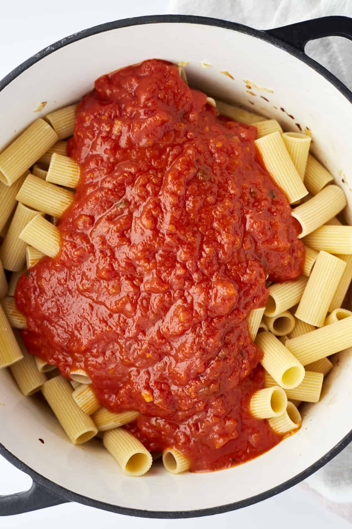 uncooked rigatoni noodles in a pot topped with marinara