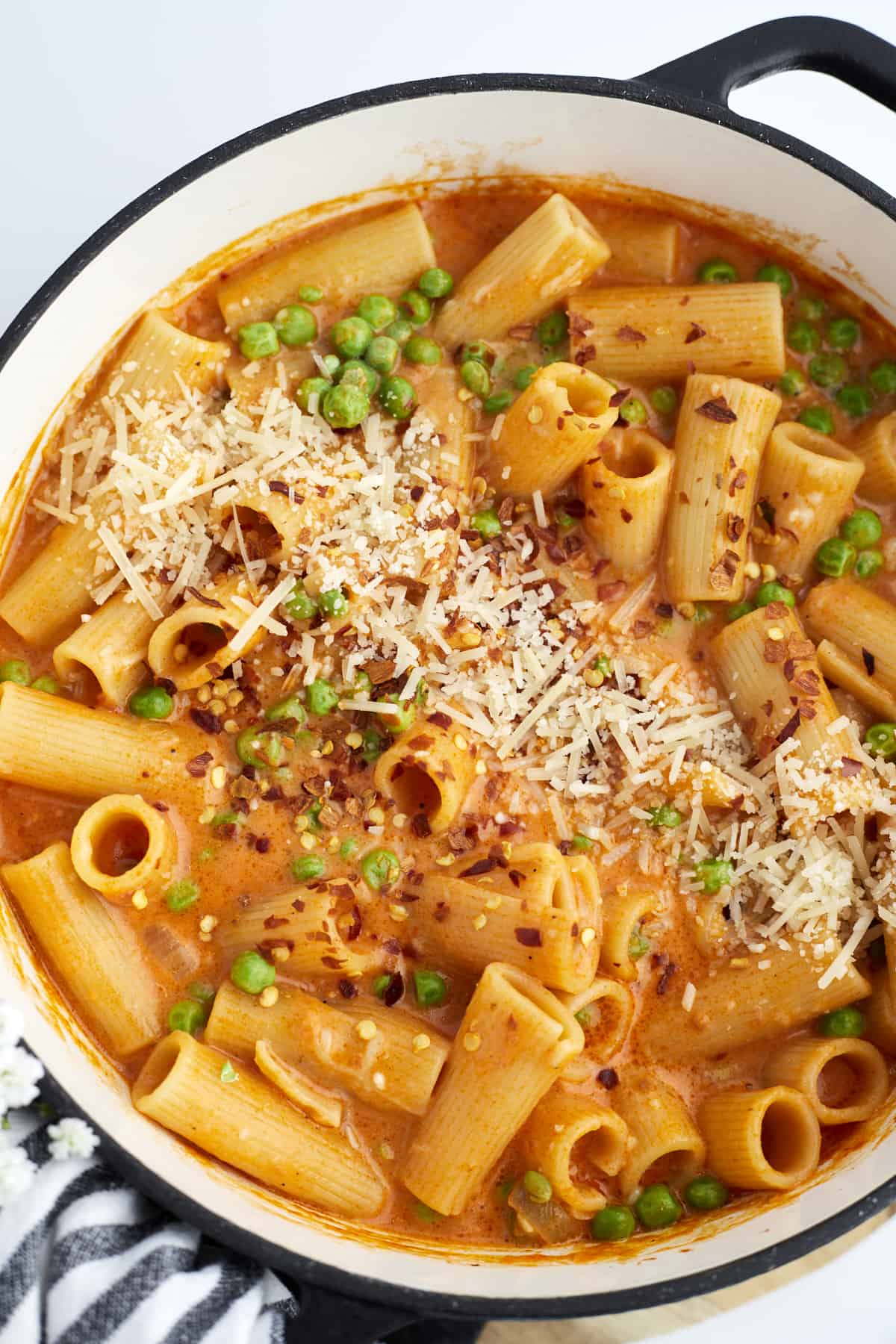 overhead image of a pot of spicy rigatoni with peas topped with shredded Parmesan