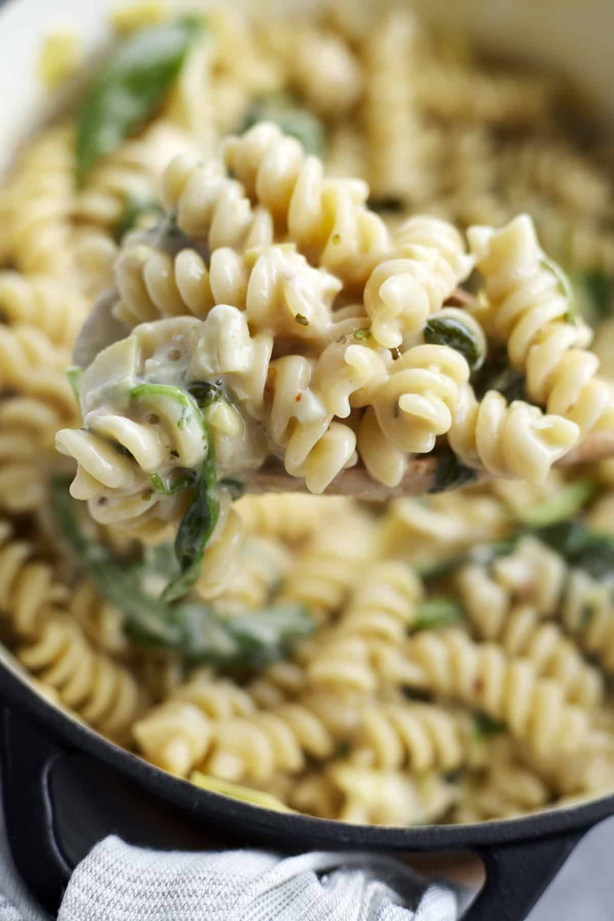 close up image of a spoonful of one pot spinach and artichoke pasta