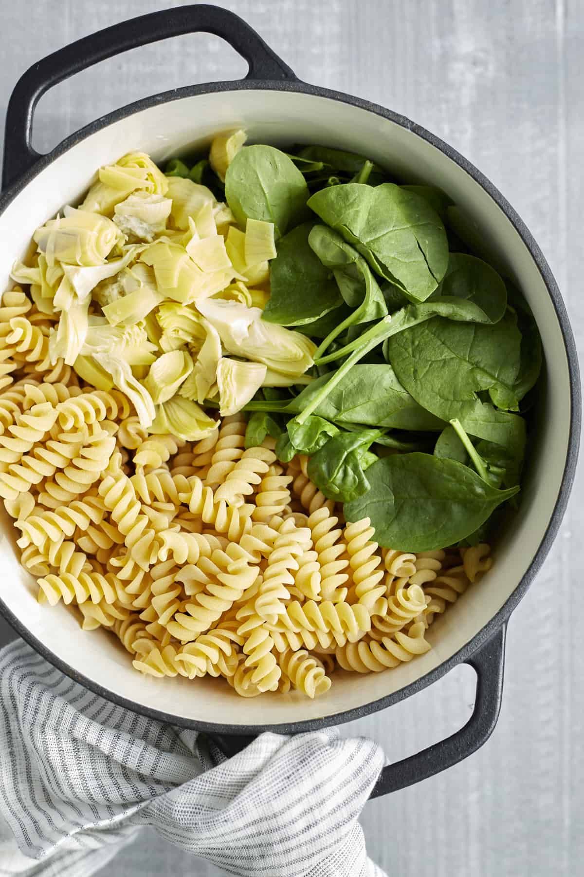 rotini noodles, spinach, and aritchoke hearts in a large pot 