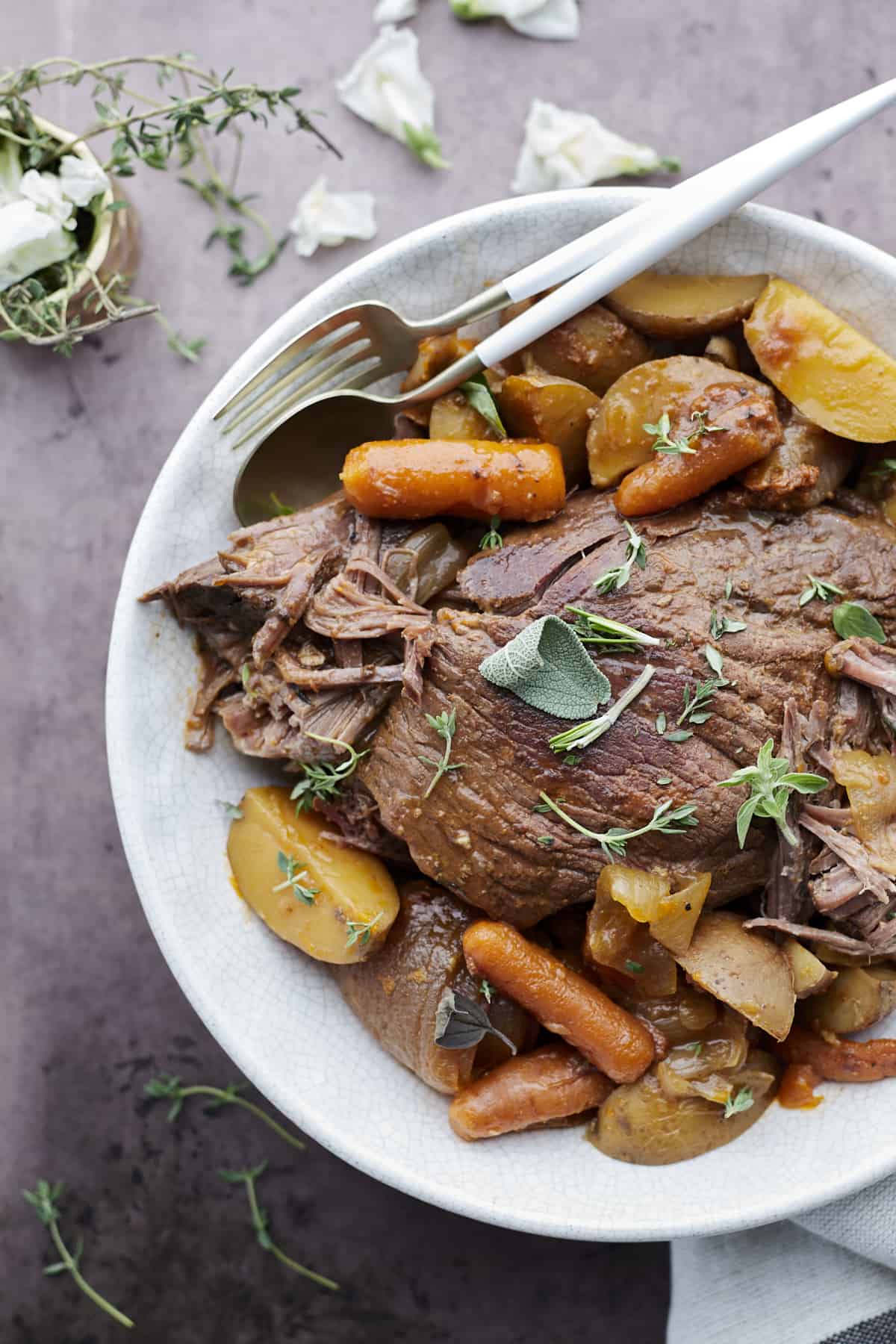 a bowl of slow cooker beef pot roast with carrots and potatoes. 