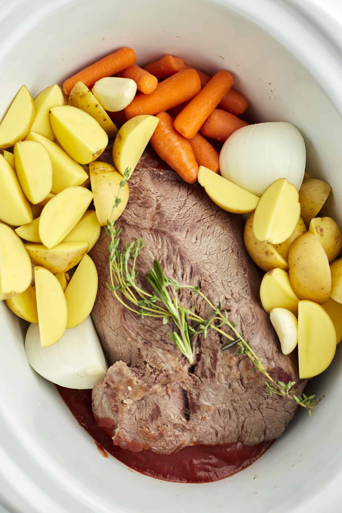 beef pot roast, golden potatoes, carrots, onions, and herbs in a slow cooker 