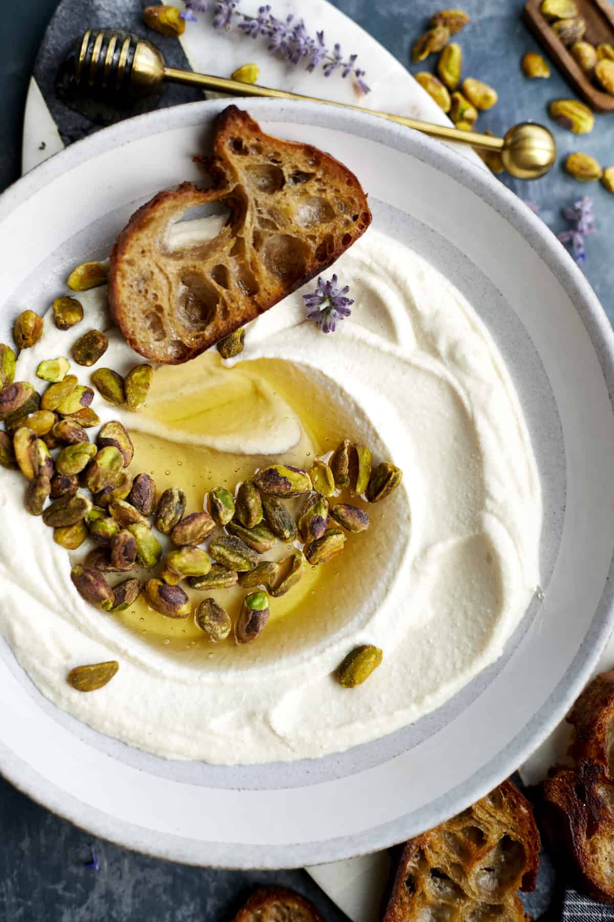 A bowl of whipped ricotta dip topped with roasted pistachios and honey with crostini.