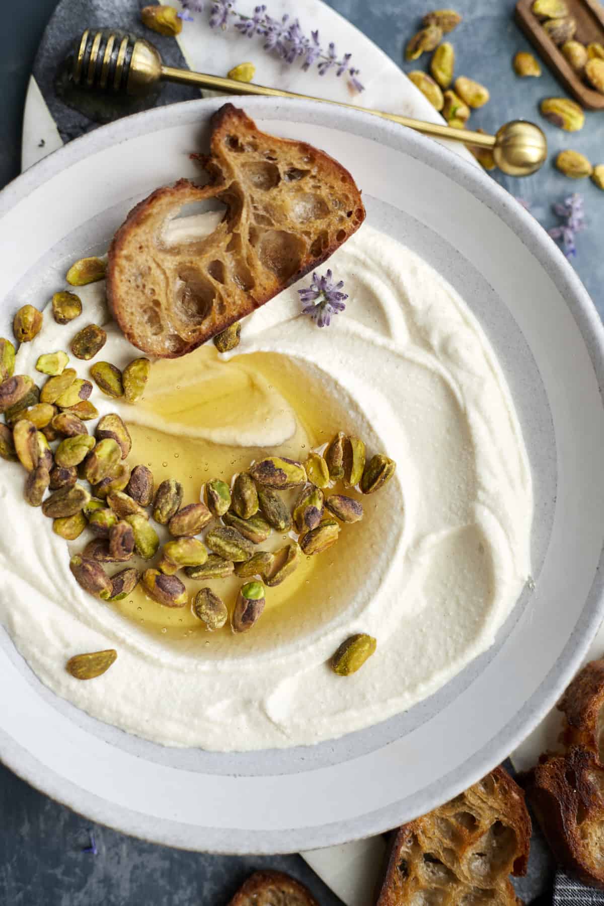 gray bowl with whipped ricotta dip, topped with pistachios, honey and crusty baguette toast
