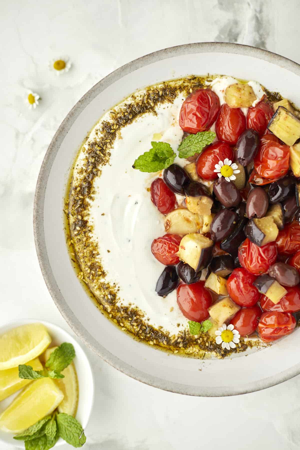 Roasted Eggplant, tomatoes, and olives plated on top of creamy yogurt dip