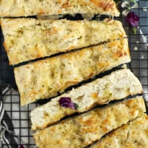 pieces of no knead cheesy focaccia bread on a cutting board with fresh basil.