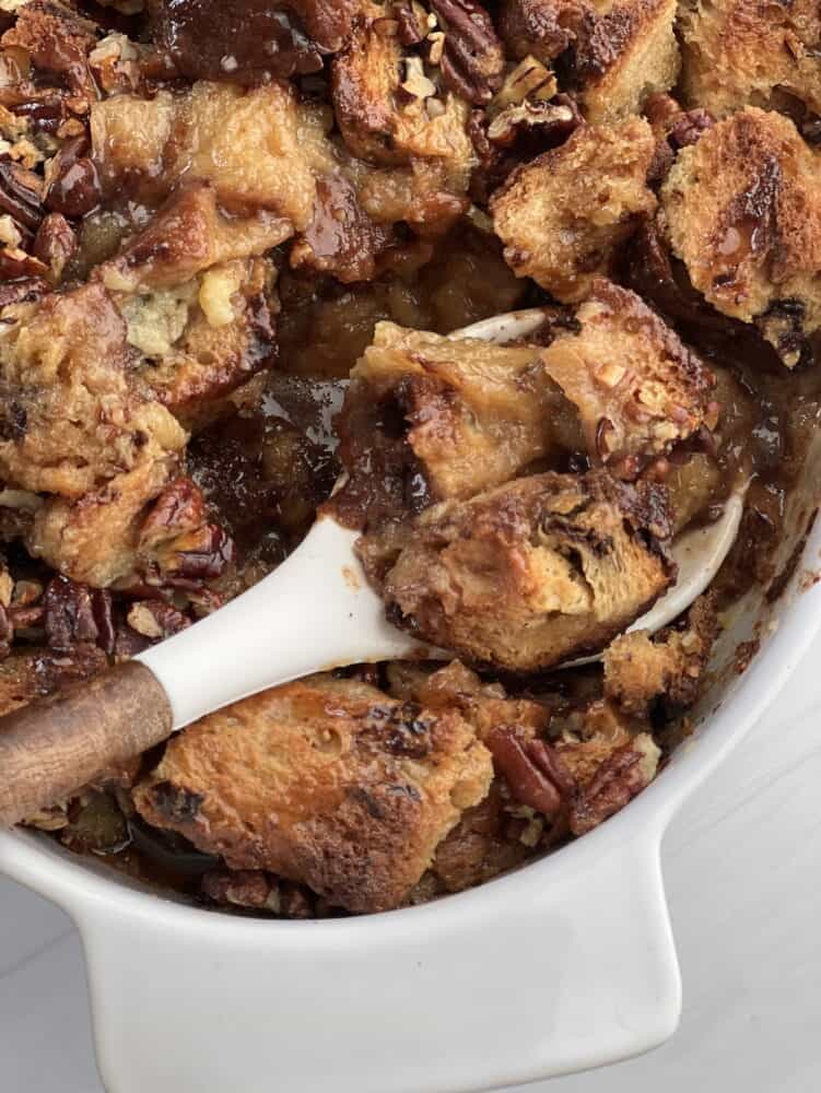 a spoon lifting a scoop of panettone bread pudding with pecan pie filling from a baking dish