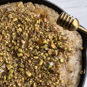 baklava skillet pancake topped with pistachios with honey being drizzled on top