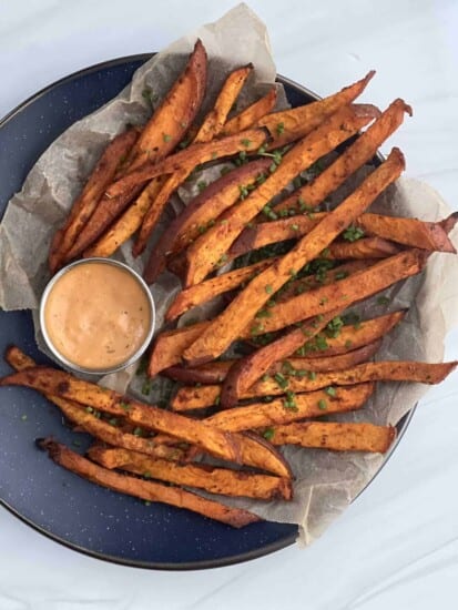 a platter of baked sweet potato fries with sauce on the side.