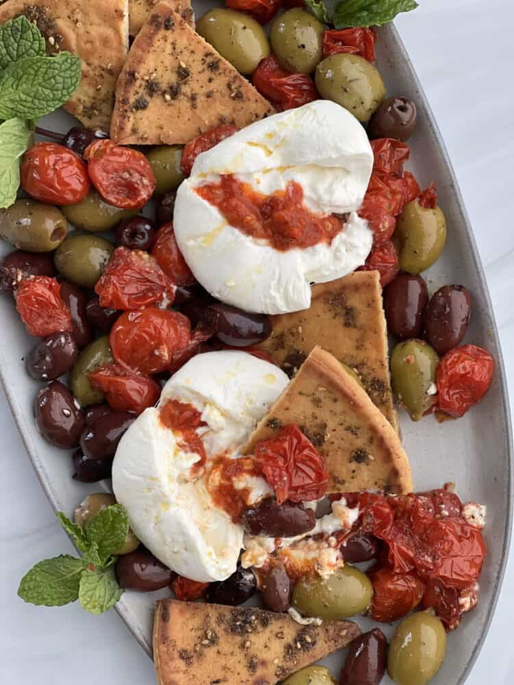 close up of burrata with roasted tomatoes, olives and zaatar pita bitten into