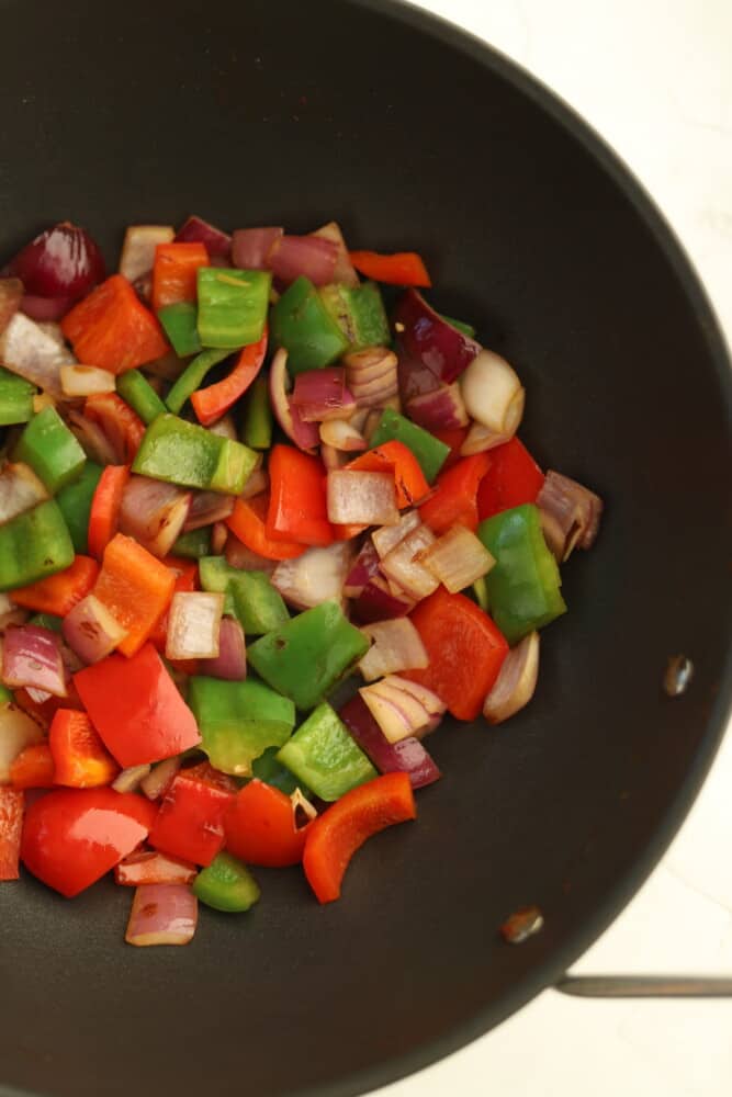 chopped red and green peppers in a wok with red onions