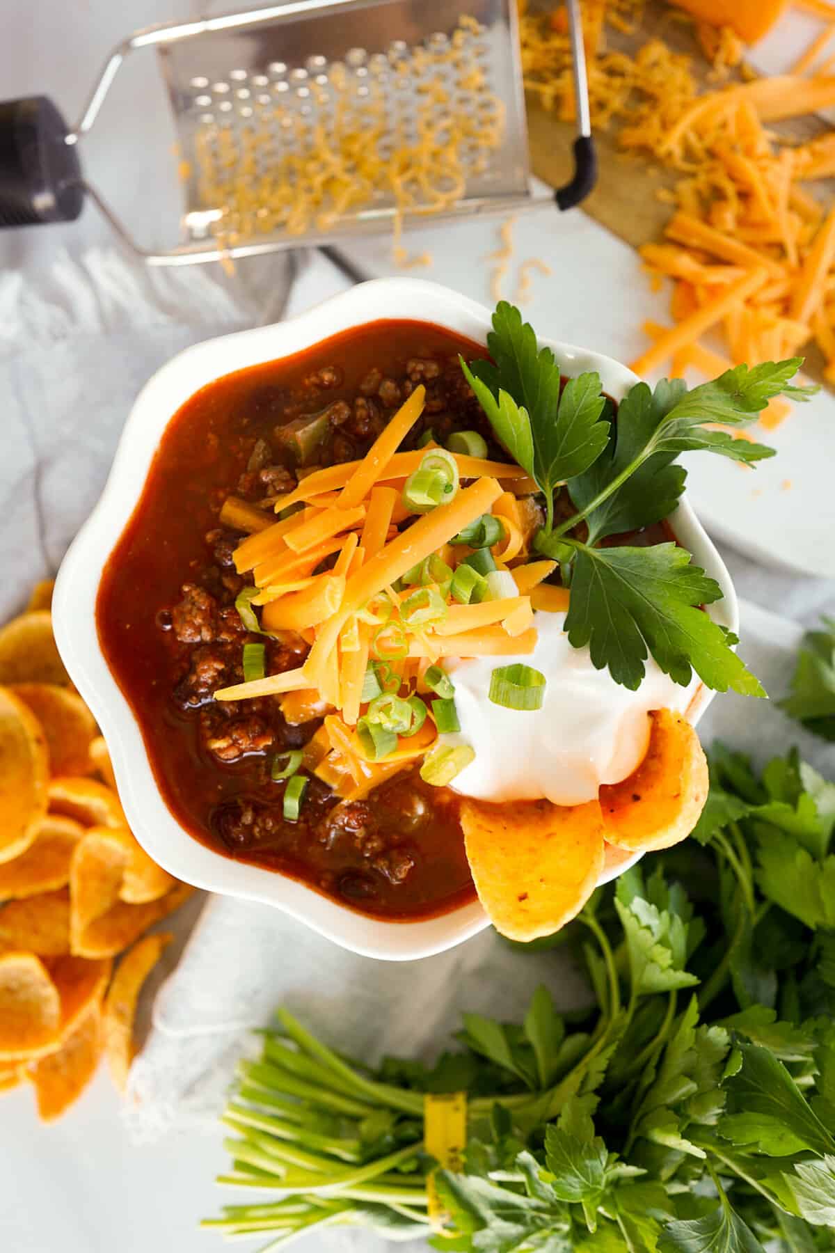 a bowl of slow cooker chili topped with shredded cheese, fresh herbs, sour cream, and a chip