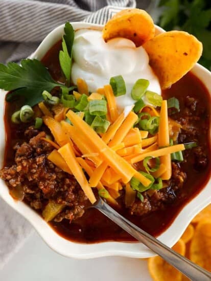 bowl of chili with sour cream, cheese, green onions and corn chips